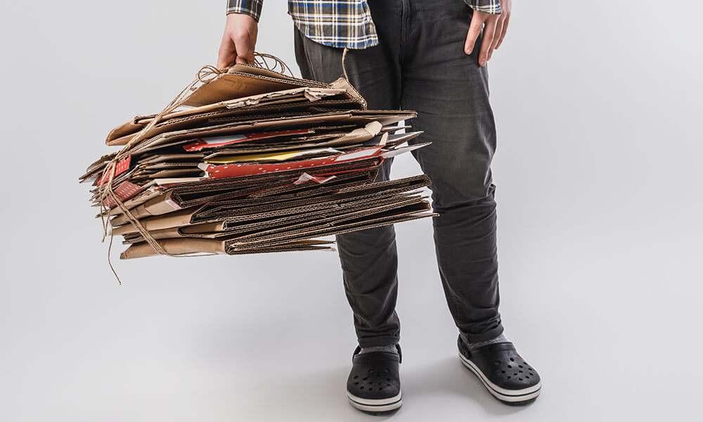 man holding bundle of flattened cardboard boxes tied up with string