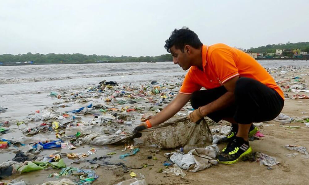 indian man cleaning up trash from the beach