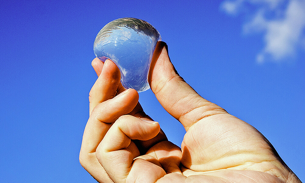 a male hand holding a water pod between his fingers in the sky