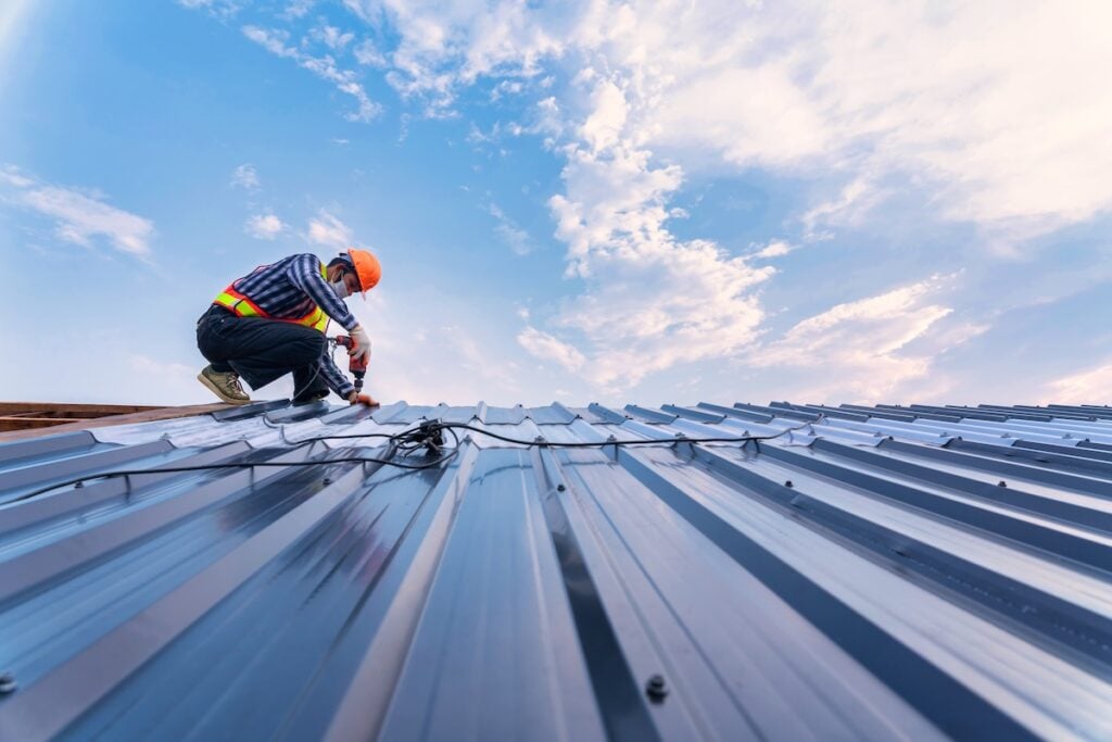 Roofer using pneumatic nail gun and installing on new roof metal sheet.