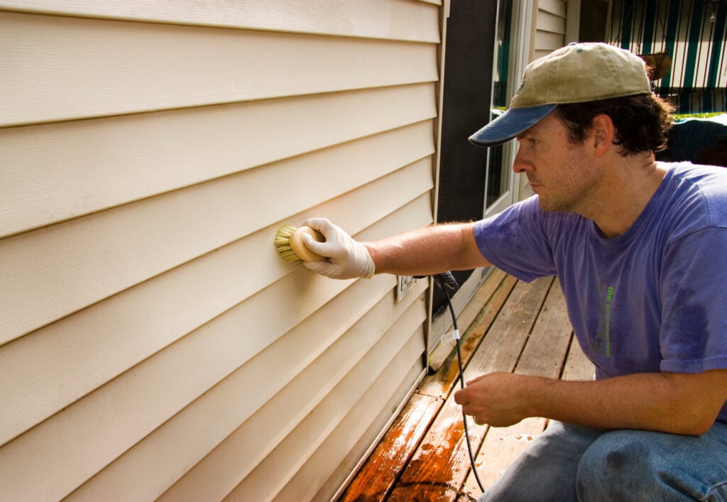 Man washing siding by hand with brush