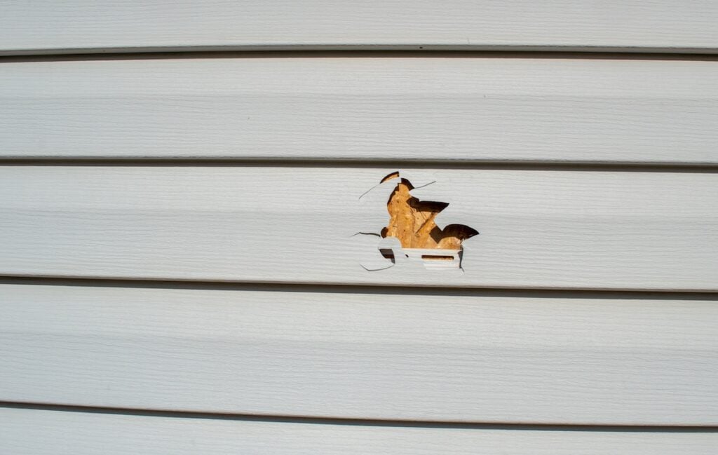 A lawnmower and a rock resulted in a punctured piece of vinyl siding on this home. Siding replacement