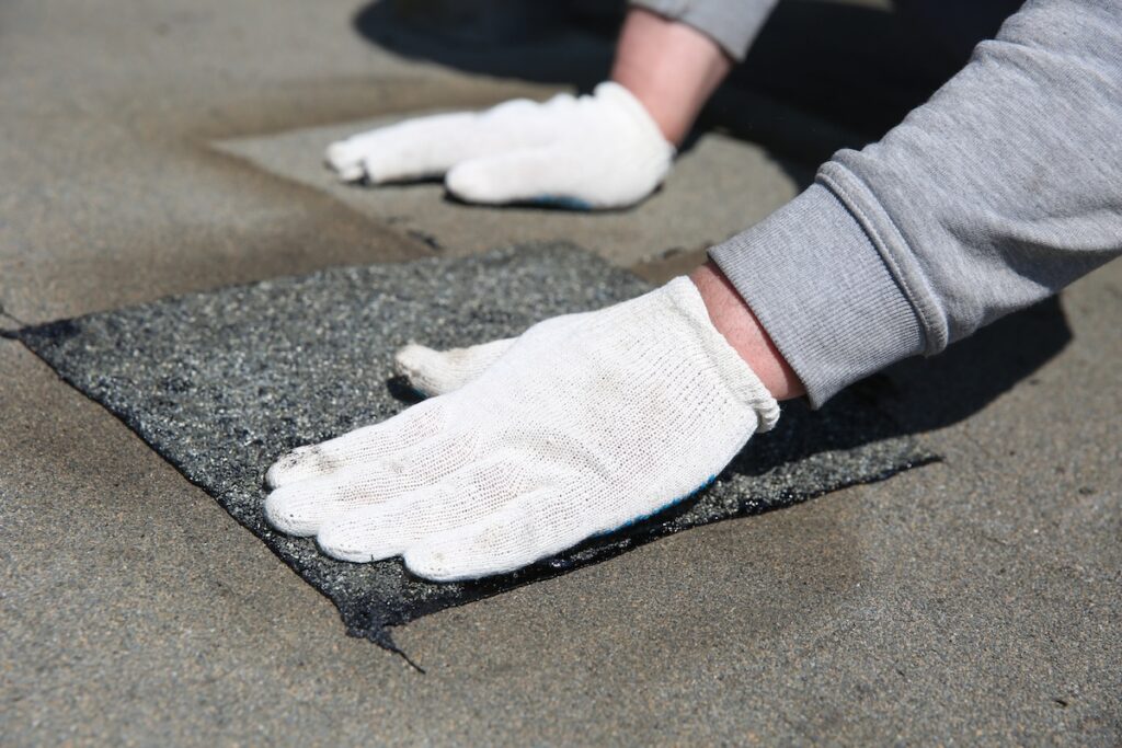 a patch of bitumen sheet for roof. local repair of roof waterproofing. hands of worker are tamping the patch on the roof