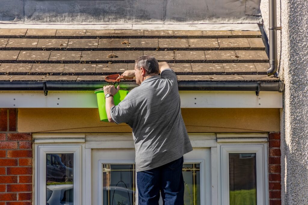 Man on ladder cleaning leaves and moss from house roof 