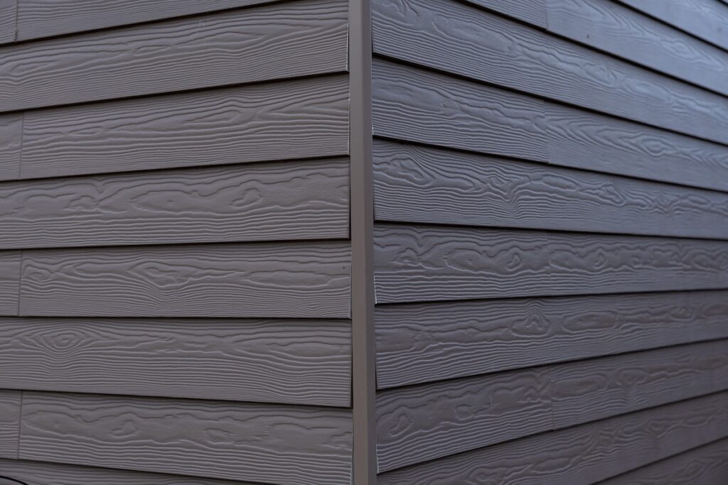The corner of a house features gray horizontal siding with a wood grain texture