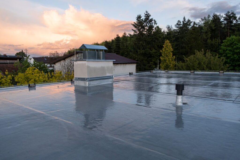 Flat roof covered with bitumen membrane and silver lacquer with chimney on a private house