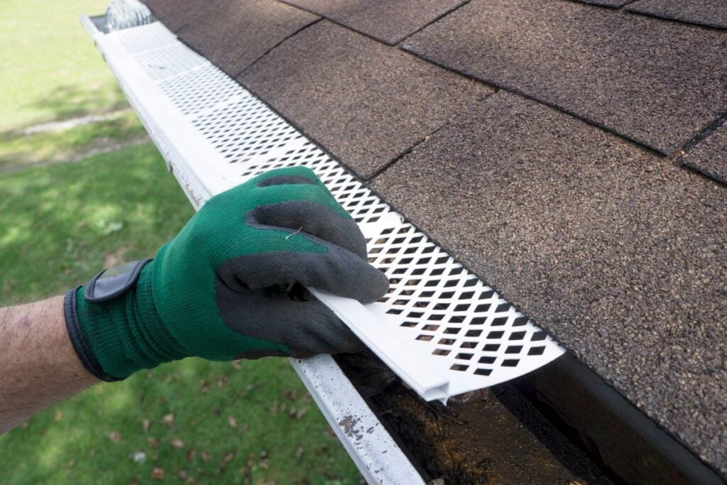 gutter guard installation green glove holding metallic guard