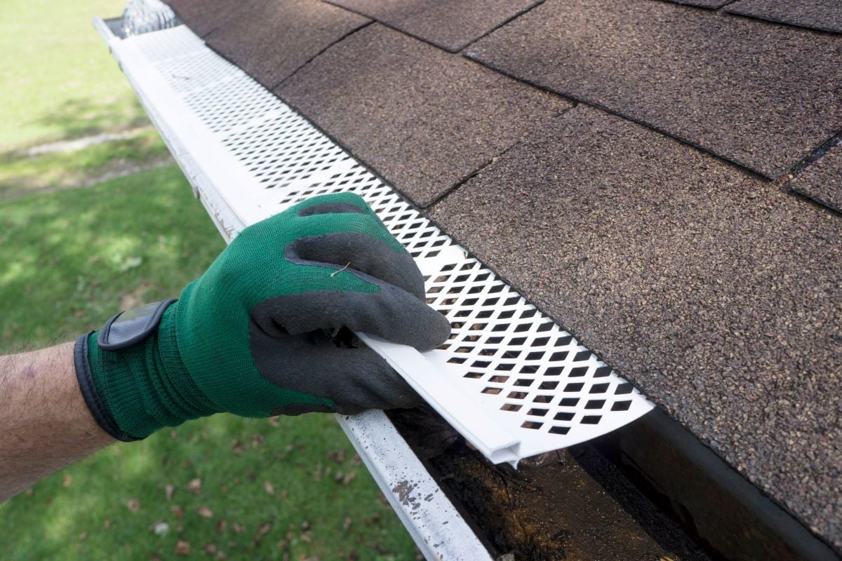 gutter guard installation green glove holding metallic guard